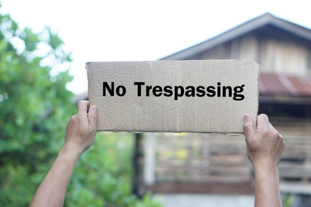 Close up hands holds No Trespassing sign, paper card in front of house. Concept, private property security, privacy, and protection for trespassing . Warning.の写真素材