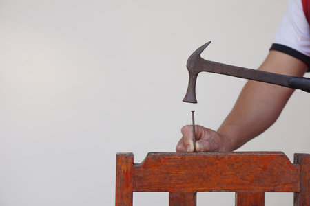 Closeup carpenter hand uses hammer to hit nail. Concept, carpentry and construction tools. Repair or fixing, DIY woodwork.の写真素材