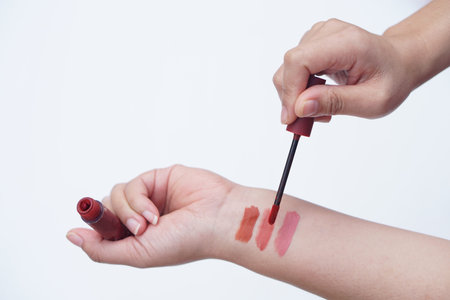 Close up woman hand is testing lip gloss different colors, apply on her arm. Lipstick swatches on...