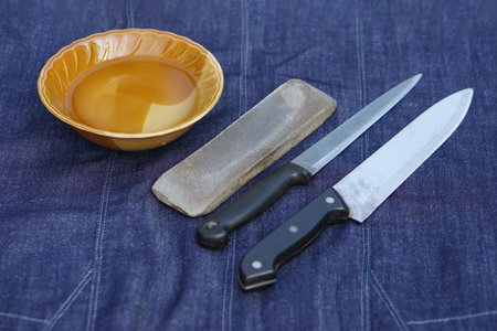 Bowl of water, grinder stone and knives, prepare for sharpening. Concept, maintenance tools for...