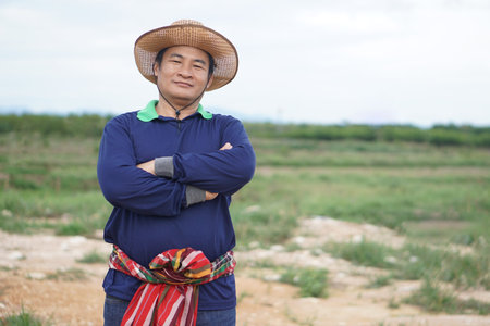 Handsome Asian man farmer stands at agricultural land, wears hat, Thai loincloth on waist, cross...