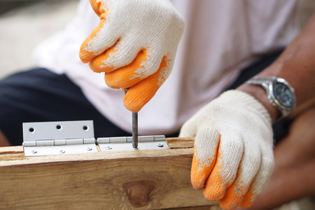Close up  carpenter hands are installing hinge on wooden window. Concept, Craft, diy, fix or repair furniture. Building materials. Construction equipment. Install in door or windowの写真素材