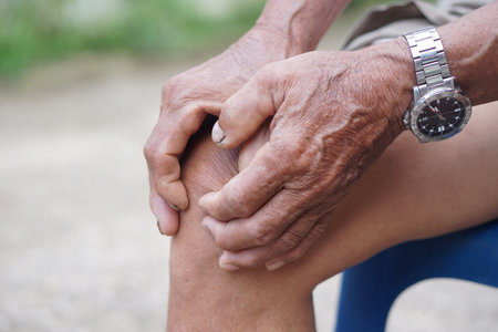 Close up elderly man hurt his knee, use hands to massage knee. Concept, health care and health problems. Artritis symptom. Suffering from knee pain. Tendon problemsの写真素材