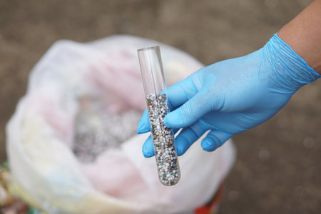 Close up hand wear blue glove hold glass tube contains sample chemical fertilizers. Concept, research the formula of chemical fertilizer production that use in agricultureの写真素材