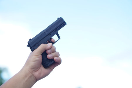 Close up hand hold black pistol gun to shoot up to the sky. Concept, dangerous violent weapon, use...