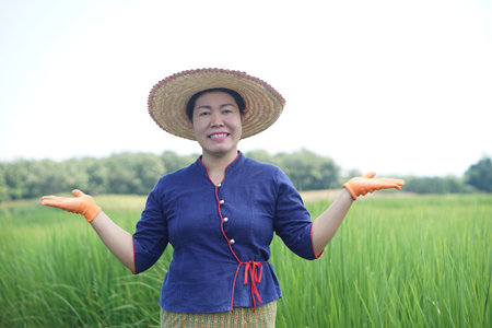 Happy Asian woman farmer is at paddy field, wear hat and gloves. Raise hands up gesture with...