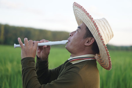 Happy Asian man farmer is playing a recorder flute at paddy field. Concept, music blowing with...