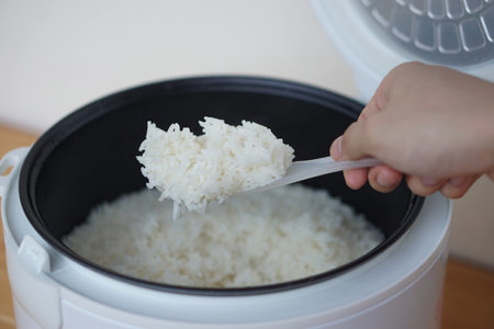 Hands use a plastic spoon to scoop rice from the electric rice cooker. Concept, cooking, checking for quality of rice before serving. everyday cuisine for living.の写真素材