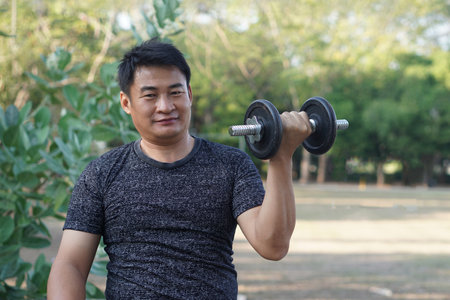 Handsome Asian man exercises outdoor, lift dumbbell. Concept, Exercise for health bodybuilding. Strengthen muscle. Weight lifting. Healthy lifestyle. Sport equipment. Work outの写真素材