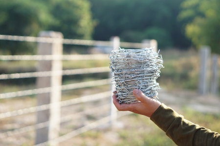 Closeup worker hand holds roll of barbed wire. Concept, construction tool. Barbed wire is used for make fences , secure property ,make border to show the territory of  area.の写真素材