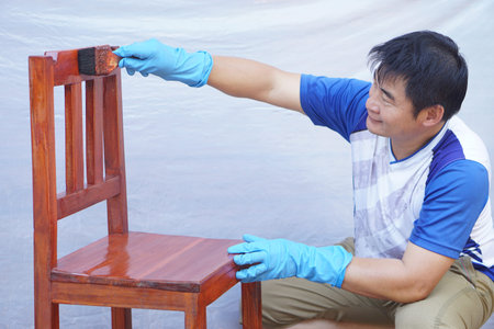 Asian man is holding brush and painting wooden chair. Concept, Repainting and maintenance for new and long live using of furniture. Renovation, Repair and diy hobby.の写真素材