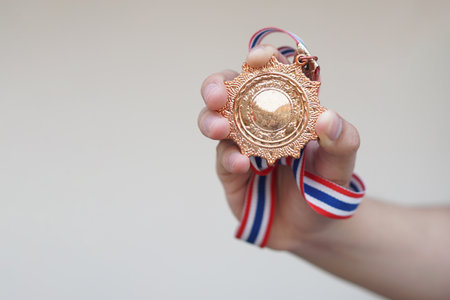Close up hand holds victory medal with red white blue ribbon strip.  from competition. Concept, symbol of win, award ,successful, pride and championship.の写真素材