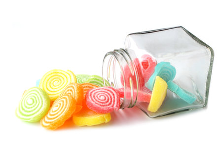 Colorful fruit-flavored jelly candies in spiral shapes spilling from a glass jar, isolated on white background. Concept for sweet snack, dessert, confectionery, childhood, sugarの写真素材