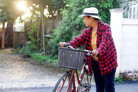 An Asian elderly woman walking her bicycle in warm afternoon light, expressing independence and an active lifestyle. Ideal for themes of healthy aging, outdoor living, and everydayの写真素材