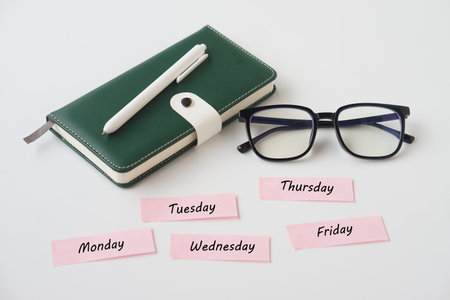 Minimal workspace with green leather planner, white pen and black eyeglasses on white background....