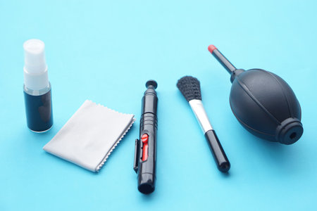 Camera lens cleaning kit with air blower, brush, spray bottle and microfiber cloth arranged on blue...