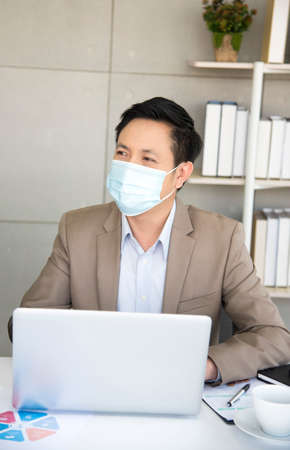 Asian male office worker wears hygienic mask on her face at work to protect from virus . Concept for New normal lifestyle at work. Awareness of wearing facemask.の写真素材