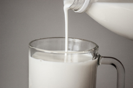 pour milk into a mug from the bottle. Whte milk on the grey background.の写真素材