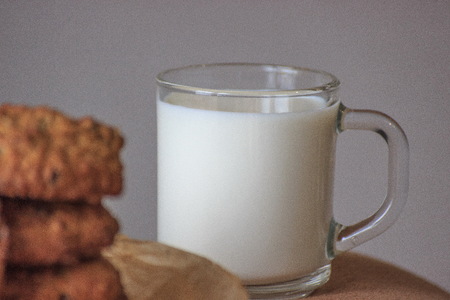 Cap of milk with oat cookies with raisins. Homemade food. Grey background. Focused on the capの写真素材