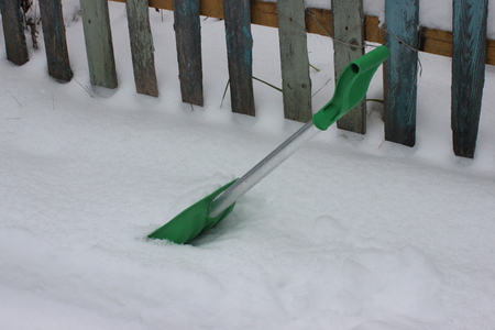 green shovel for snow removal in the yard of a private house. clean the path at entrance to the gate in snowy winter.の写真素材