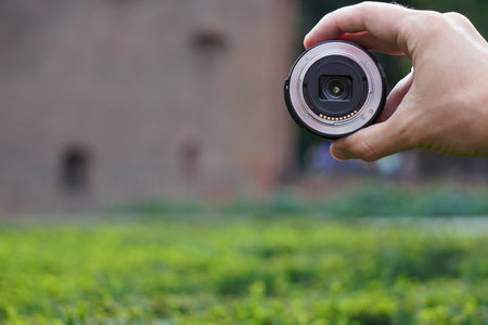 photo lens in the hand of man against city on background of green and red brick wall. modern...