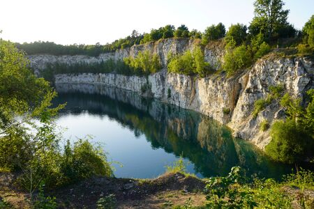 rocky shore stone quarry with grass and shrubs. water is dark green with reflection of stones. lake after development of the resourceの写真素材