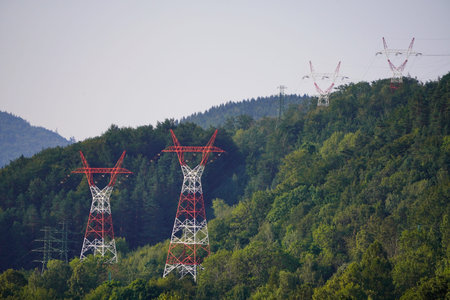 High-voltage power line. red and white power poles in a hilly green forest. transmission of...