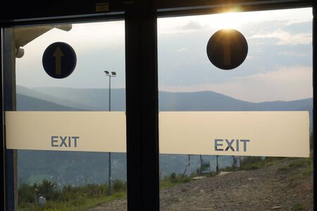 doors with stickers with exit information on the background of mountains and forests, misty sky and sunlight. exit in clouds and mountains.の写真素材