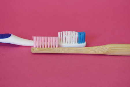 the wooden and plastic toothbrushes on coral or purple background. natural materials in everyday...