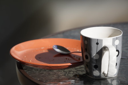 coral plate with crumbs and Cup stand on a glass table on a Sunny day. after meals, dirty dishes before cleaningの写真素材