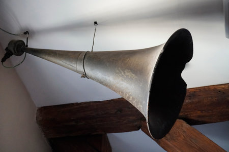 old metal loudspeaker suspended from the ceiling ofwooden house, white ceiling