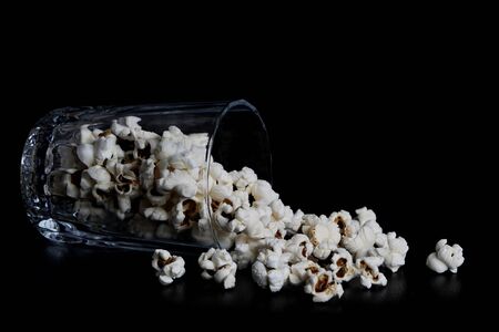 popcorn spilled from a glass on a black background. Scattered, on his back in a glass. photo in low keyの写真素材