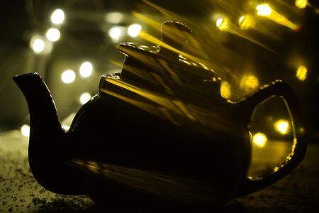 the shadow of the kettle on dark background and light bulbs. Dark background. Vintage black ceramic teapot.の写真素材