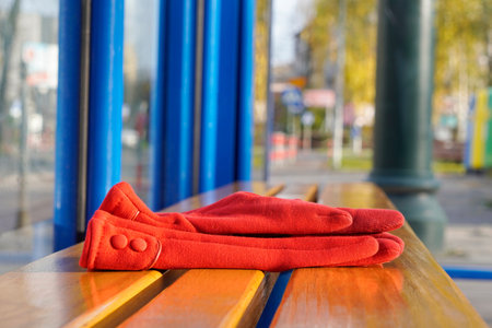 red women's gloves forgotten on a bench or at a bus stop on warm Sunny day. warehouse or lost and...