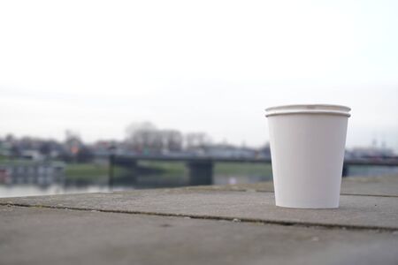 a white paper Cup stands on a concrete railing against the blurred backdrop of the bridge and the city. takeaway coffee in a disposable bowl, zero weist.の写真素材