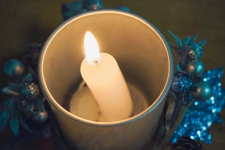 burning Christmas candle in a candlestick decorated with festive Christmas decorations. Blue backlight, open candle flameの写真素材