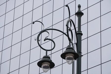 city lantern in the old style against the blue modern glass facade of an office building, street lighting in the city. a combination of old and newの写真素材