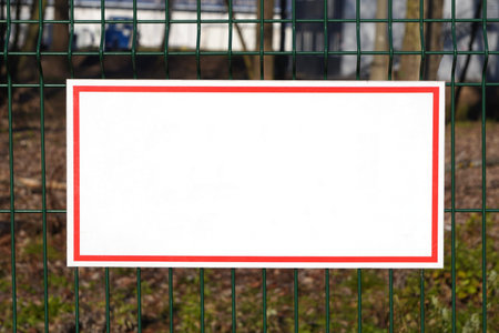 blank white sign with a red border on the green fence in the forest, copyspace . empty white table on the fence of a protected object, protected areaの写真素材