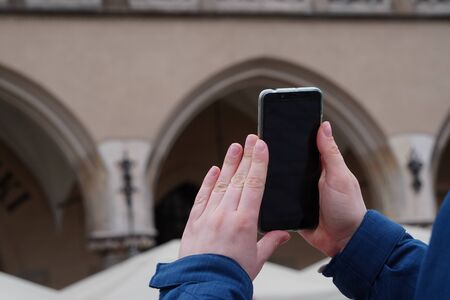 Hand of tourist holding mobile smartphone with black screen on background of an old house, photographing sights or architecture. Journeys or Travel concepts and technologyの写真素材