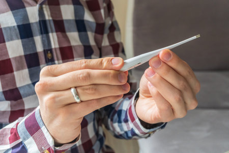 White electronic thermometer in the hands of a man. High body temperature. Symptoms of coronavirus...