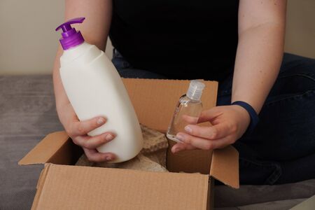 A girl or young woman lays out parcel with a mask, disinfectant and soap. Contactless delivery during a coronavirus pandemic. Being at home, in quarantine. Social distance and isolationの写真素材