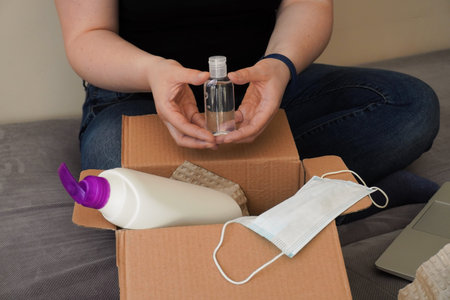A girl or young woman lays out parcel with a mask, disinfectant and soap. Contactless delivery...