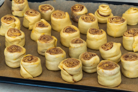 Preparation of the rolls or buns with cinnamon and sugar. Raw Rolled rolls stand on baking paper on...