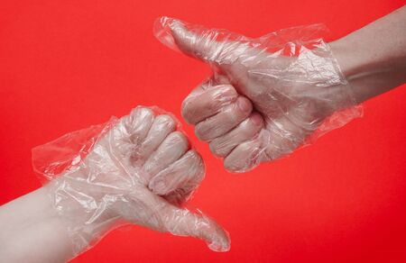 Two hands in plastic or rubber protective disposable gloves on red background. Protection against viruses and bacteria during coronavirus pandemic.Thumbs up sign, copy space, ok or like sign concept.の写真素材