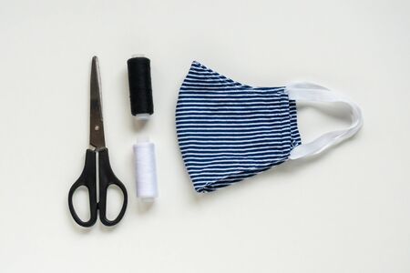 Sewing reusable and washable cotton mask during coronavirus or infection or allergy. Thread, scissors, and blue-and-white striped mask on white background.DIY, Handmade product.の写真素材