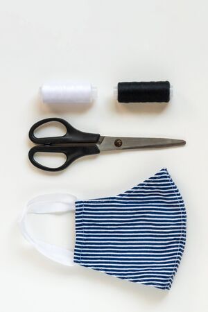 Sewing reusable and washable cotton mask during coronavirus or infection or allergy. Thread, scissors, and blue-and-white striped mask on white background. DIY, Handmade product.の写真素材