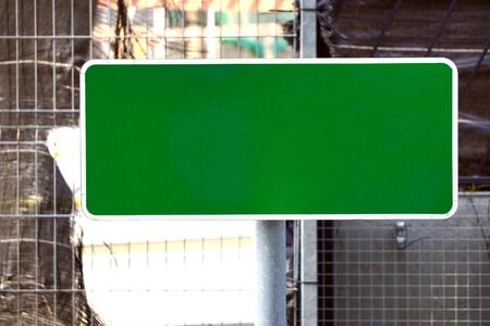 Green placard with a place for text on the fence against the background of city in focus. Blank green banner for advertisement mockup mountedの写真素材