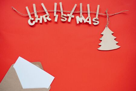 Christmas flatley, wooden word Christmas and a Christmas tree hanging on a string on bright red background with craft envelope and white paper inside for notes. natural decoration for the holidays.の写真素材