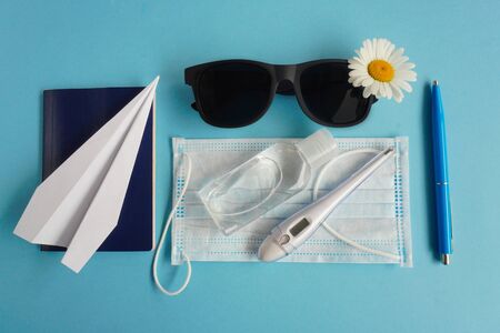 Summer layout with daisies and sunglasses, airplane-origami, sanitizer, passport and medical mask. Concept of travel and recreation. Flights to sea, rest during coronavirus.Flatlay on blueの写真素材