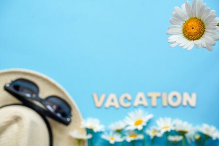 Blurred: straw hat with sunglasses and white flowers daisies on blue background, one Daisy is in focus. Summer flatlay background with traveler accessories.Top view with copy-space. Vacation conceptの写真素材